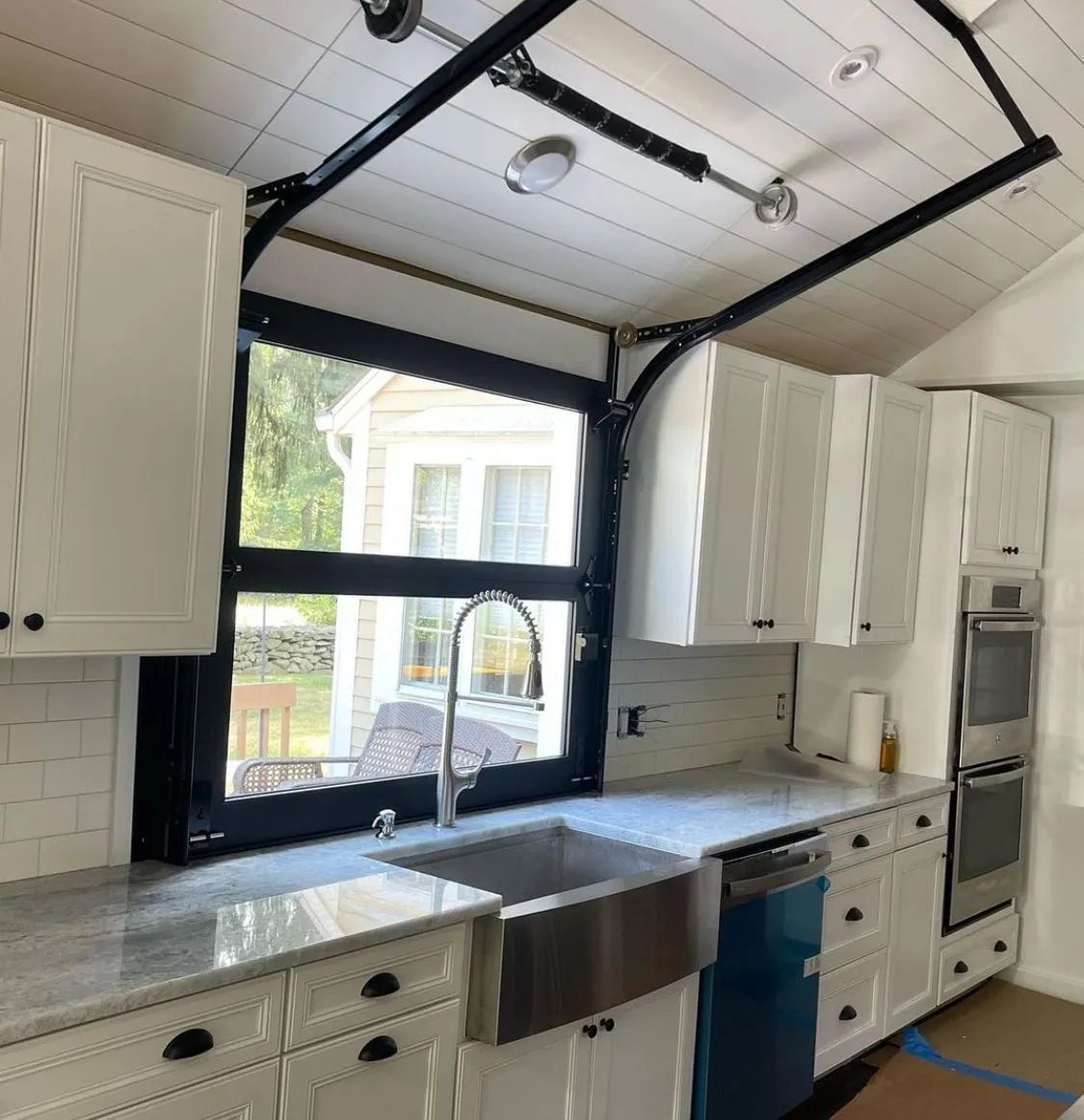 Bright white kitchen with black-framed windows, farmhouse sink, and white cabinets under a sloped ceiling.