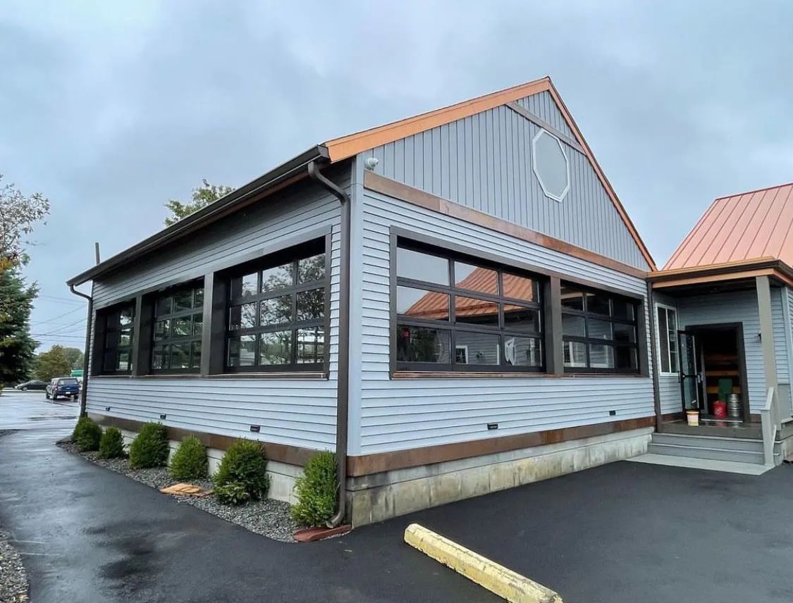 Modern gray building with orange roof trim and large windows beside a wet driveway
