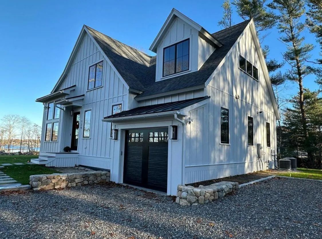 White two-story house with a black garage door, steep gables, and a gravel driveway under a clear blue sky