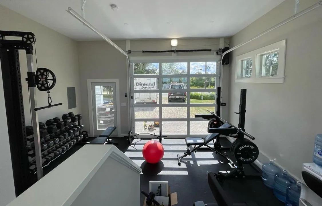 Small home gym with weights, bench, rowing machine, and a red exercise ball by glass doors.