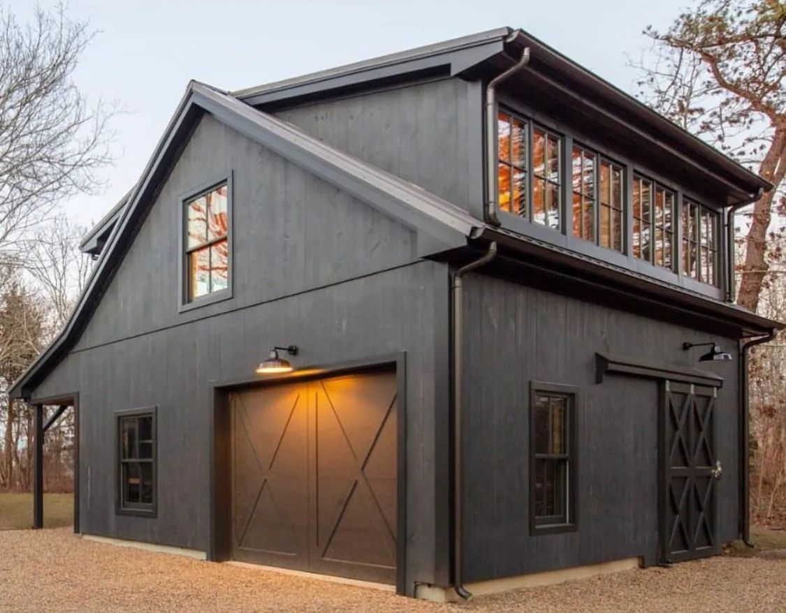 Dark gray barn-style house with warm-lit garage door and upper balcony windows