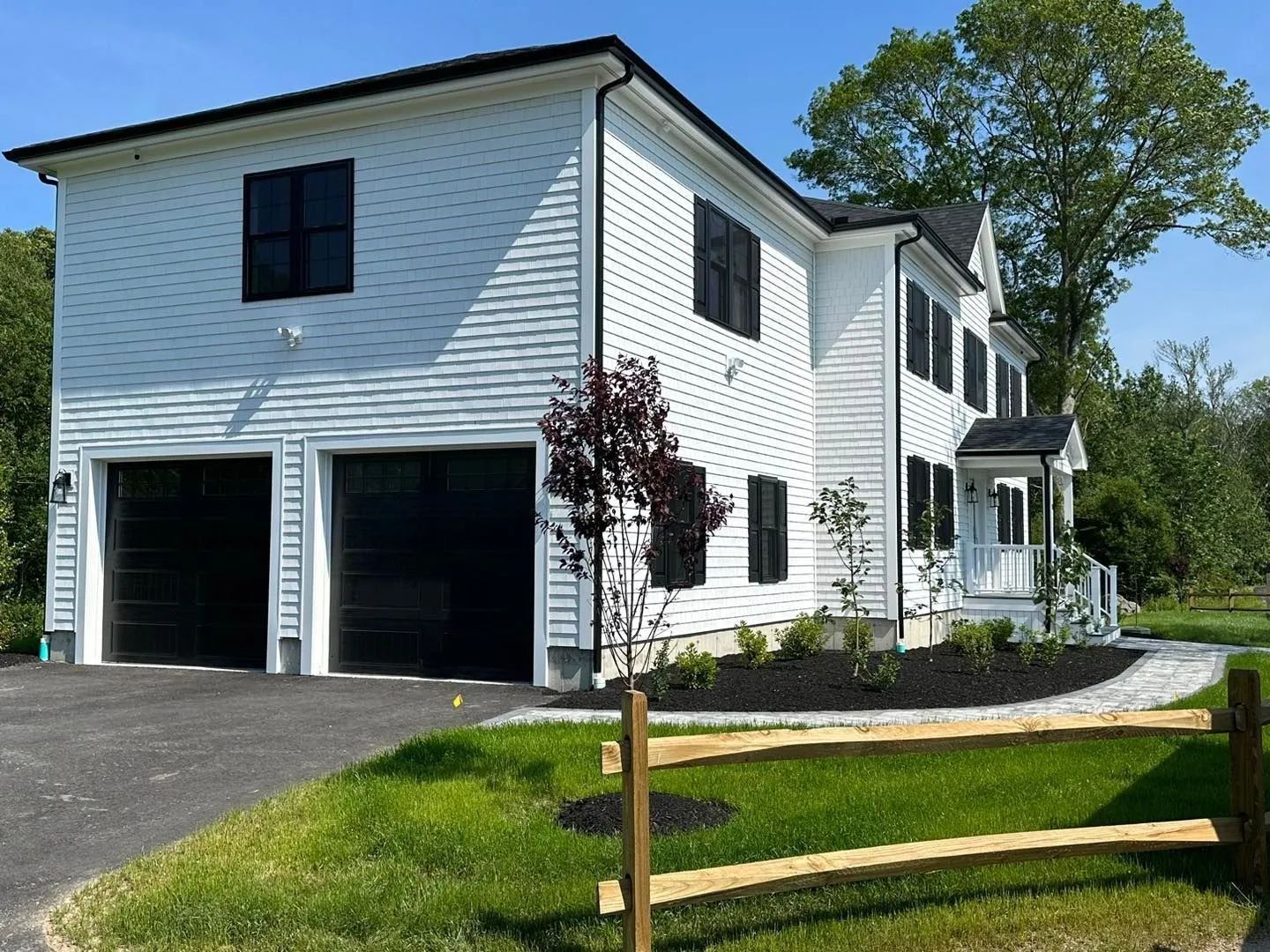 White two-story house with attached garage, black shutters, and a front lawn by a wooden fence