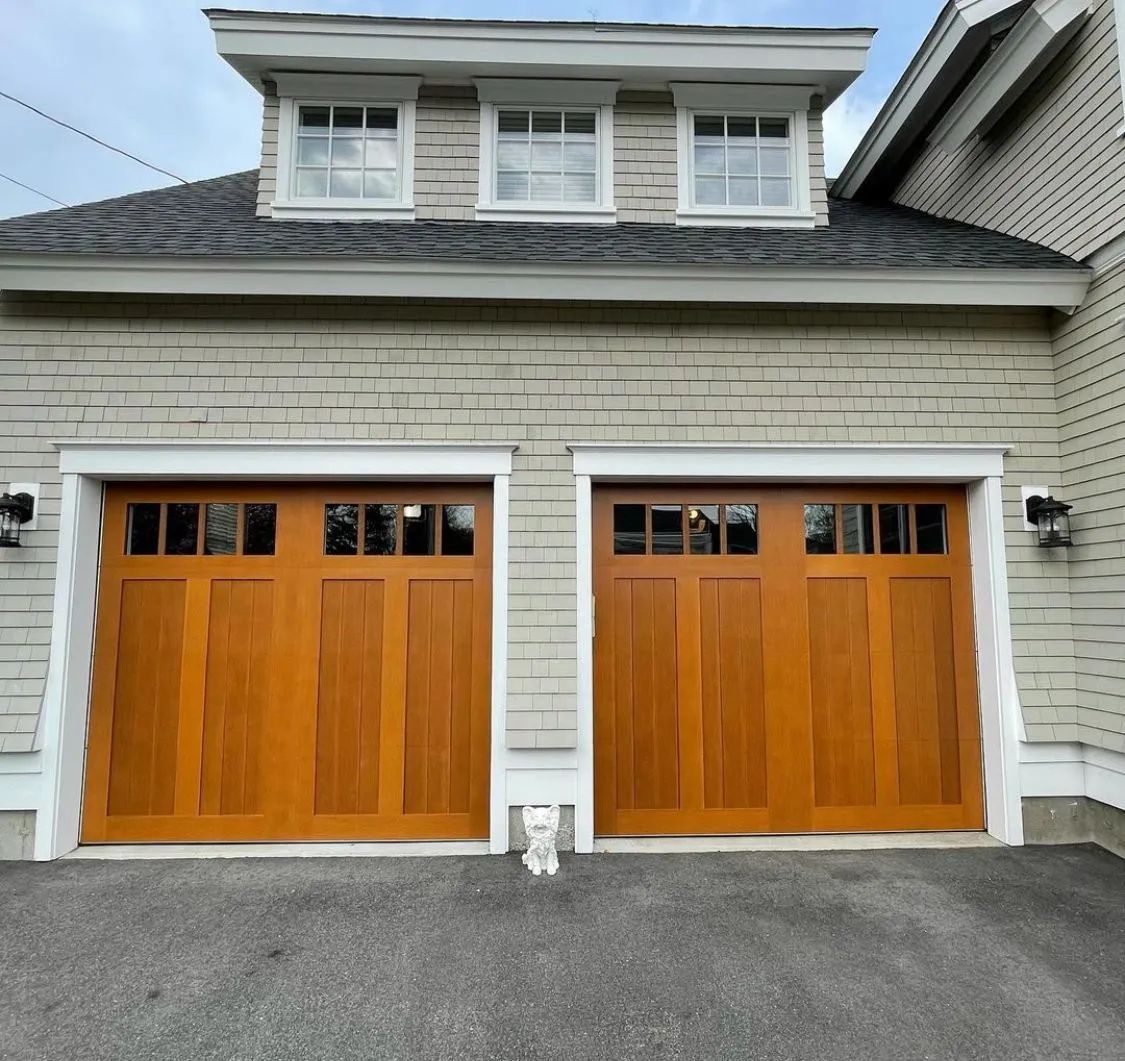 Two wooden garage doors on a gray house with white trim and a dormer above