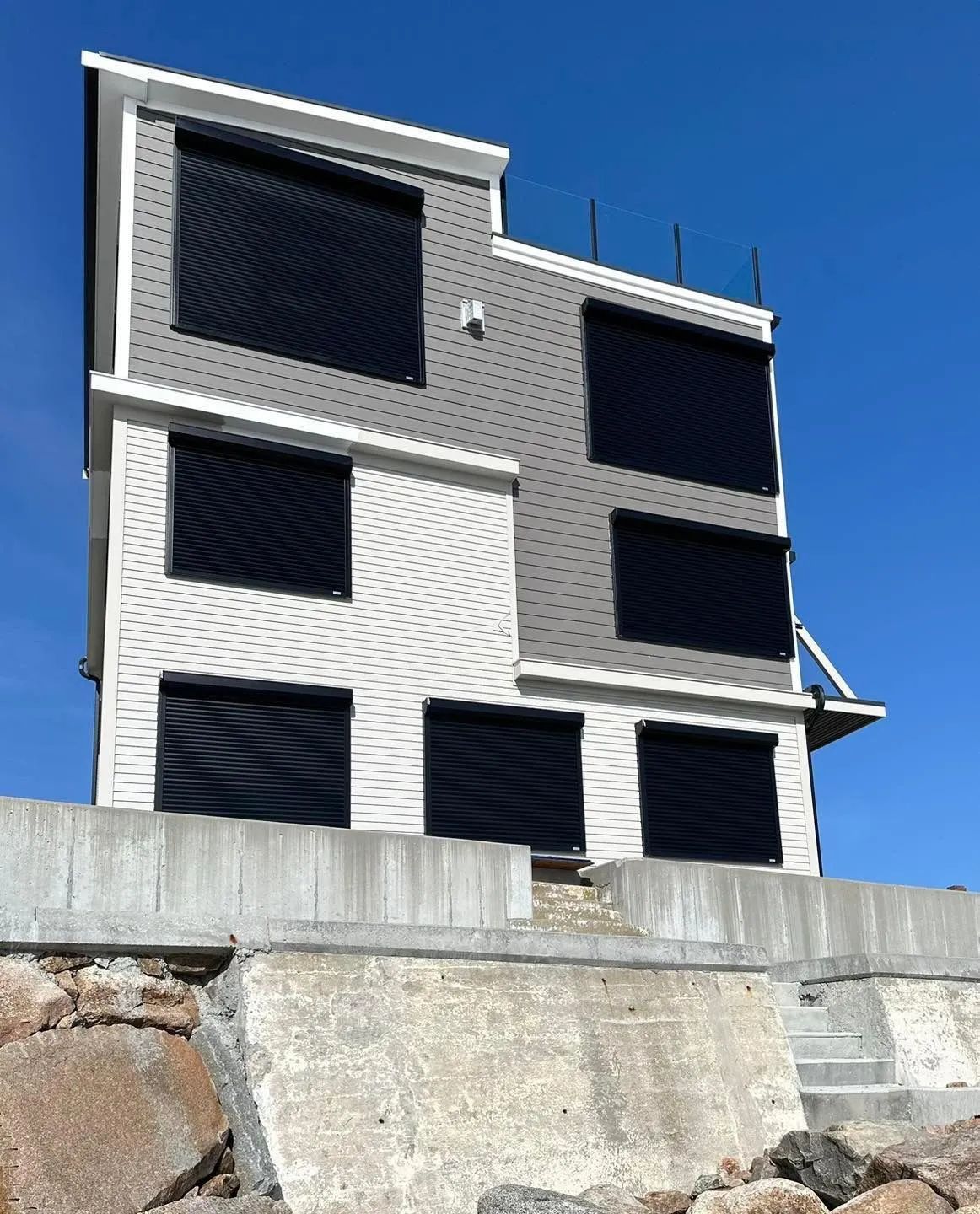 Modern multi-story building with dark shutters behind a concrete wall under a clear blue sky