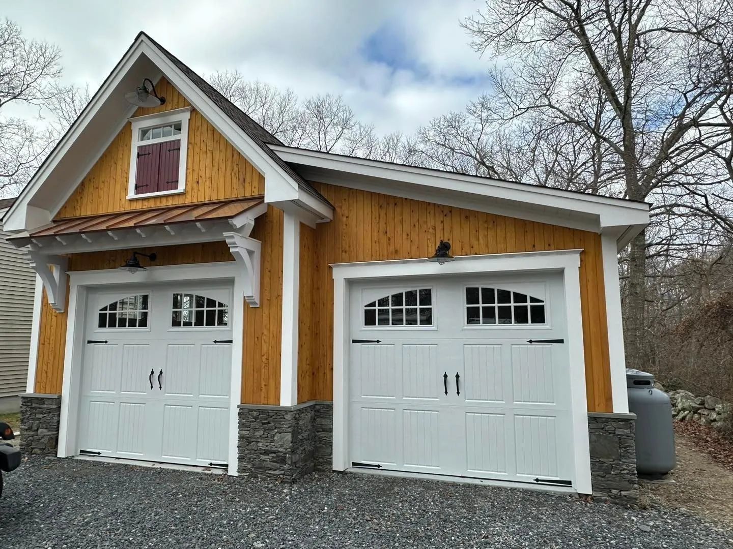 Two-car garage with white doors, yellow siding, and stone base under a cloudy sky.