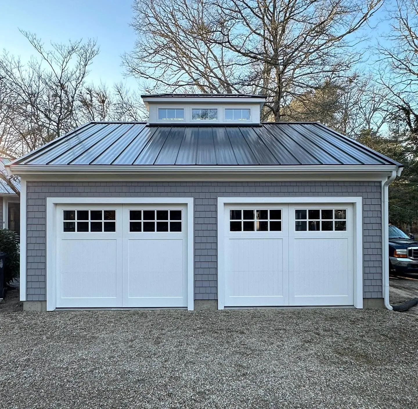 Gray two-car garage with white doors and a metal roof in a gravel driveway