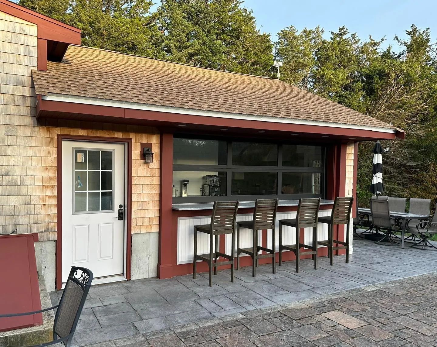 Outdoor patio bar with stools beside a white door and stone wall under a tiled roof