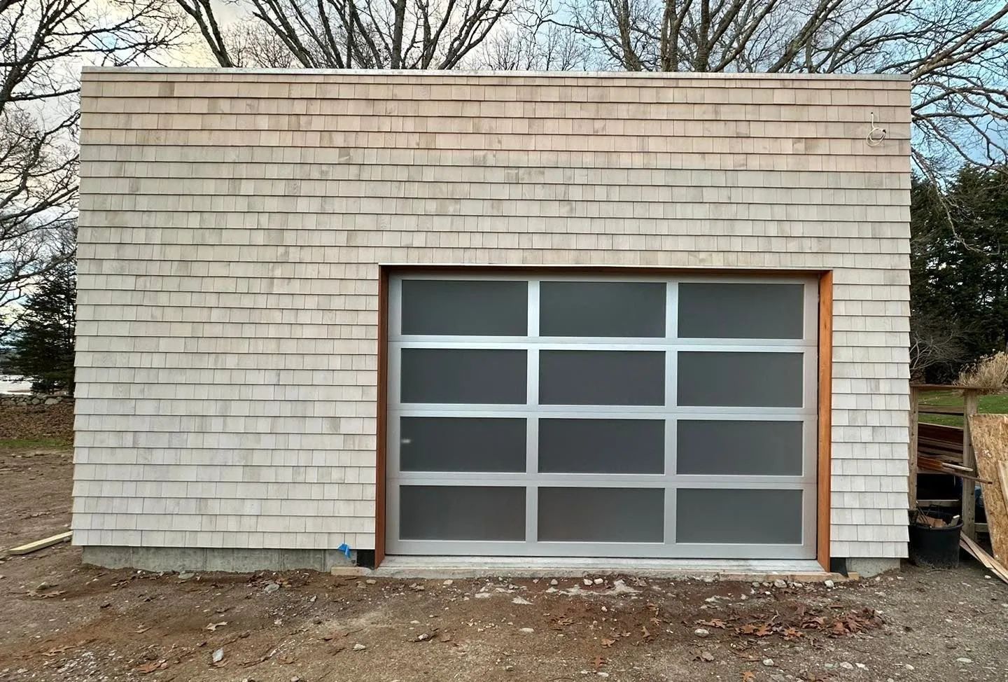 Small brick building with a gray glass garage door and bare trees in the background