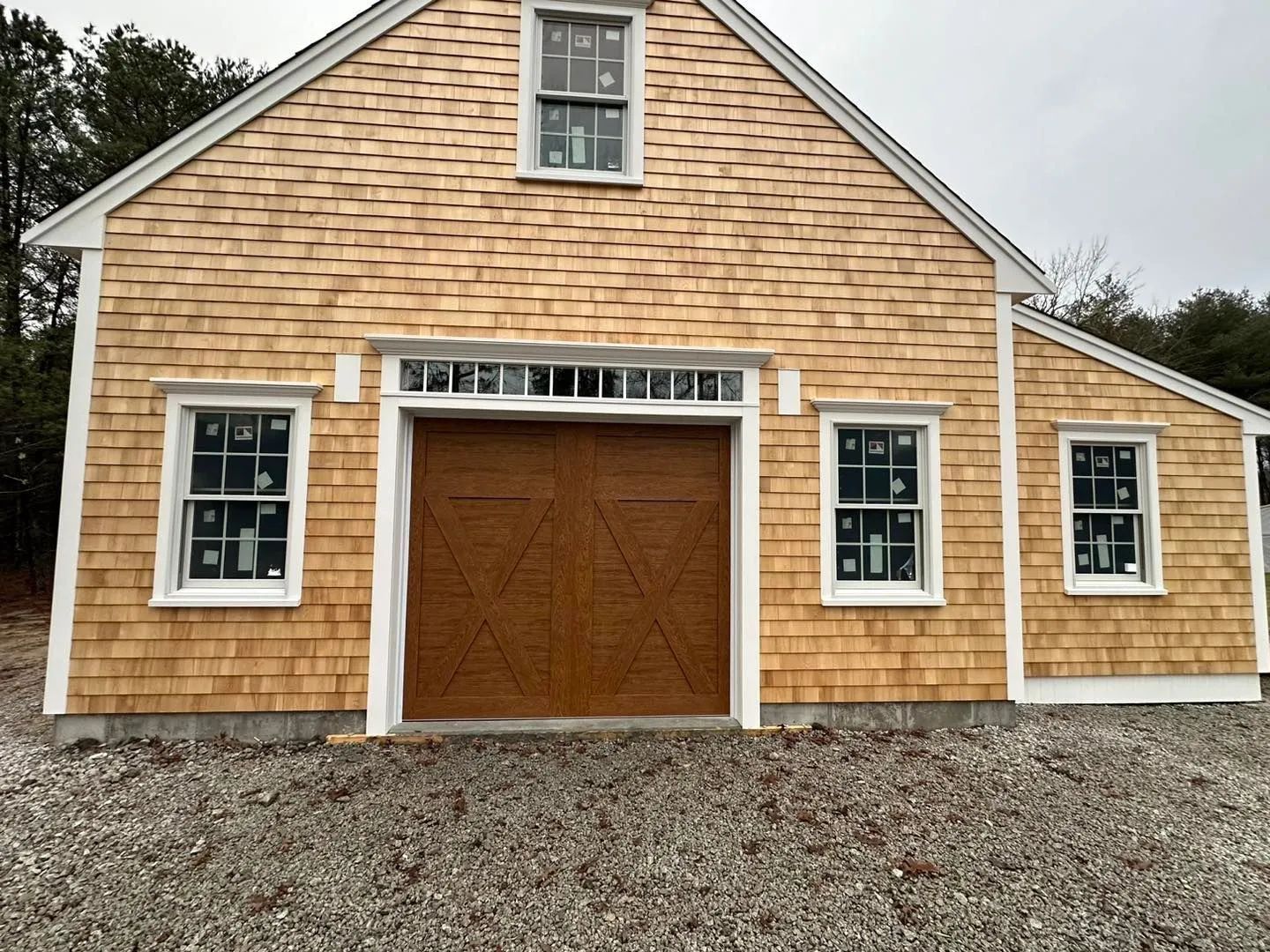 Front view of a tan shingle barn with large wooden doors and gravel driveway