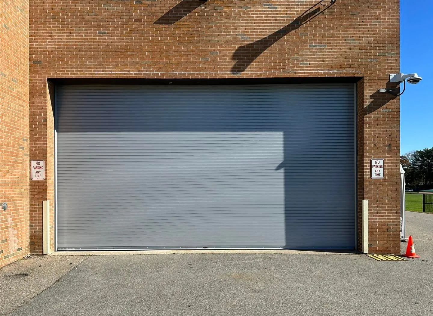 Closed gray roller garage door on a brick building with a gravel driveway and traffic cones nearby