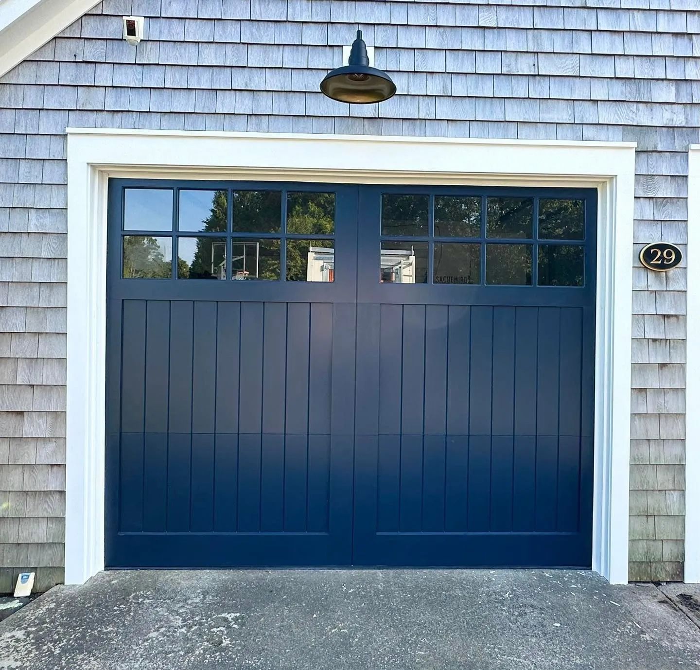 Blue garage door with white trim and small windows on a shingled house exterior