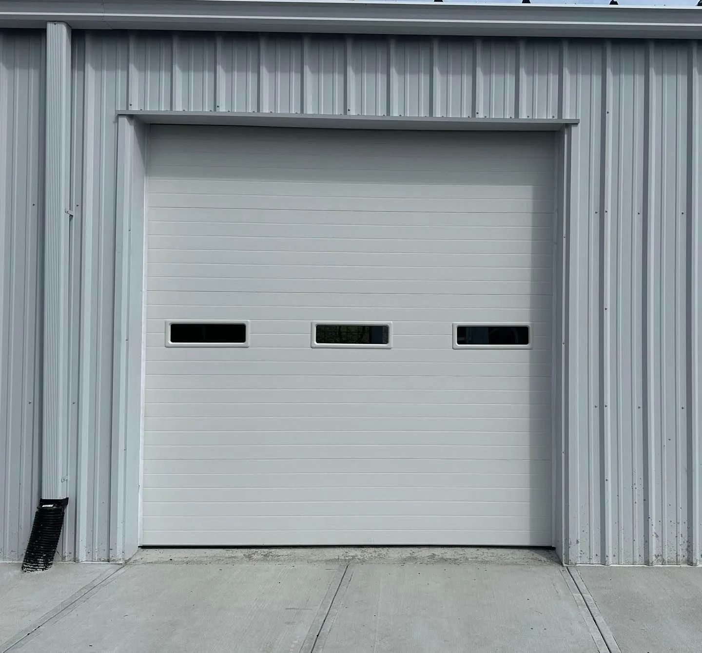 Gray industrial garage door with three narrow windows in a metal building facade