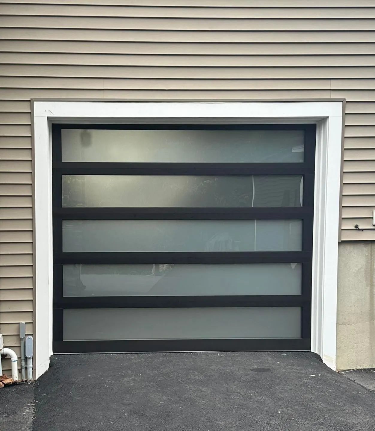 Modern black garage door with frosted glass panels on a beige house exterior