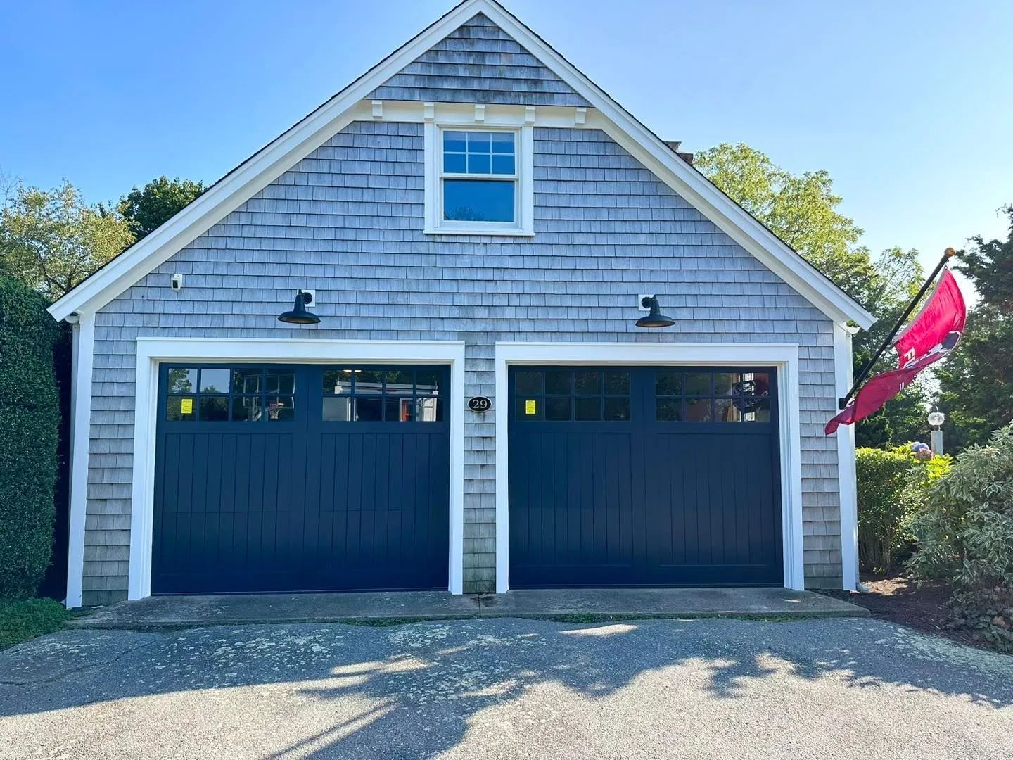 Blue-gray garage with two dark blue doors, white trim, and a small red flag on the right side.