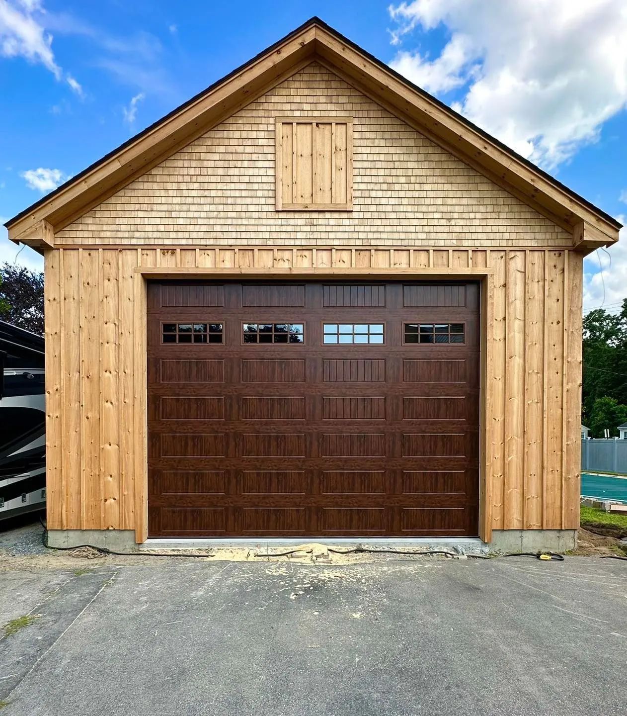 Wooden garage with tan siding and a dark brown roll-up door, viewed from the driveway.