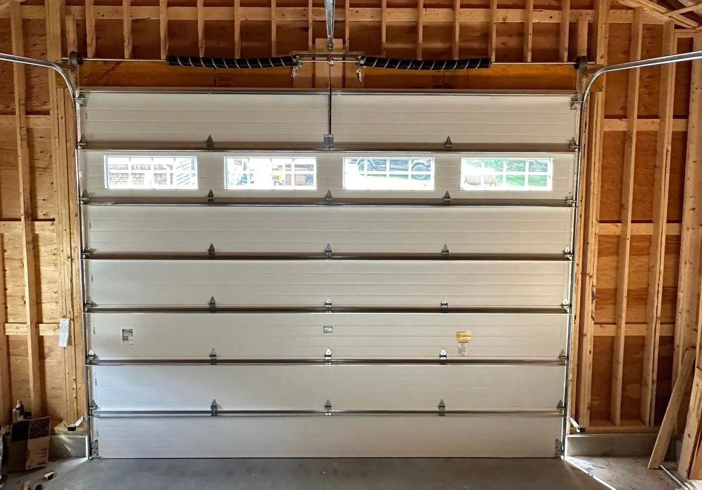 Interior view of an unfinished garage with a white sectional door and exposed wooden framing