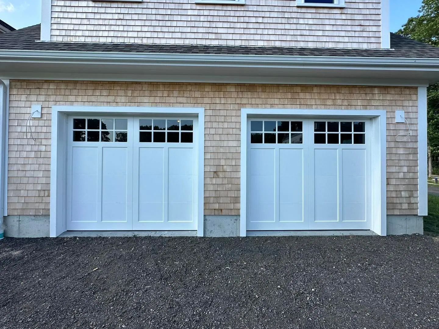 Two white garage doors on a house with shingle siding and a gravel driveway