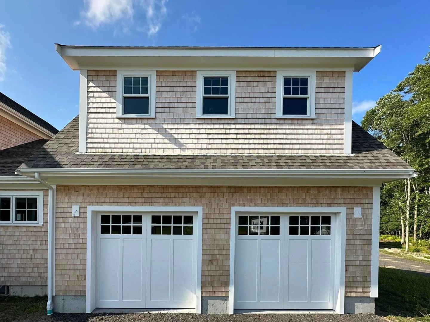 Two-story beige shingle house with white trim and double garage doors under a blue sky