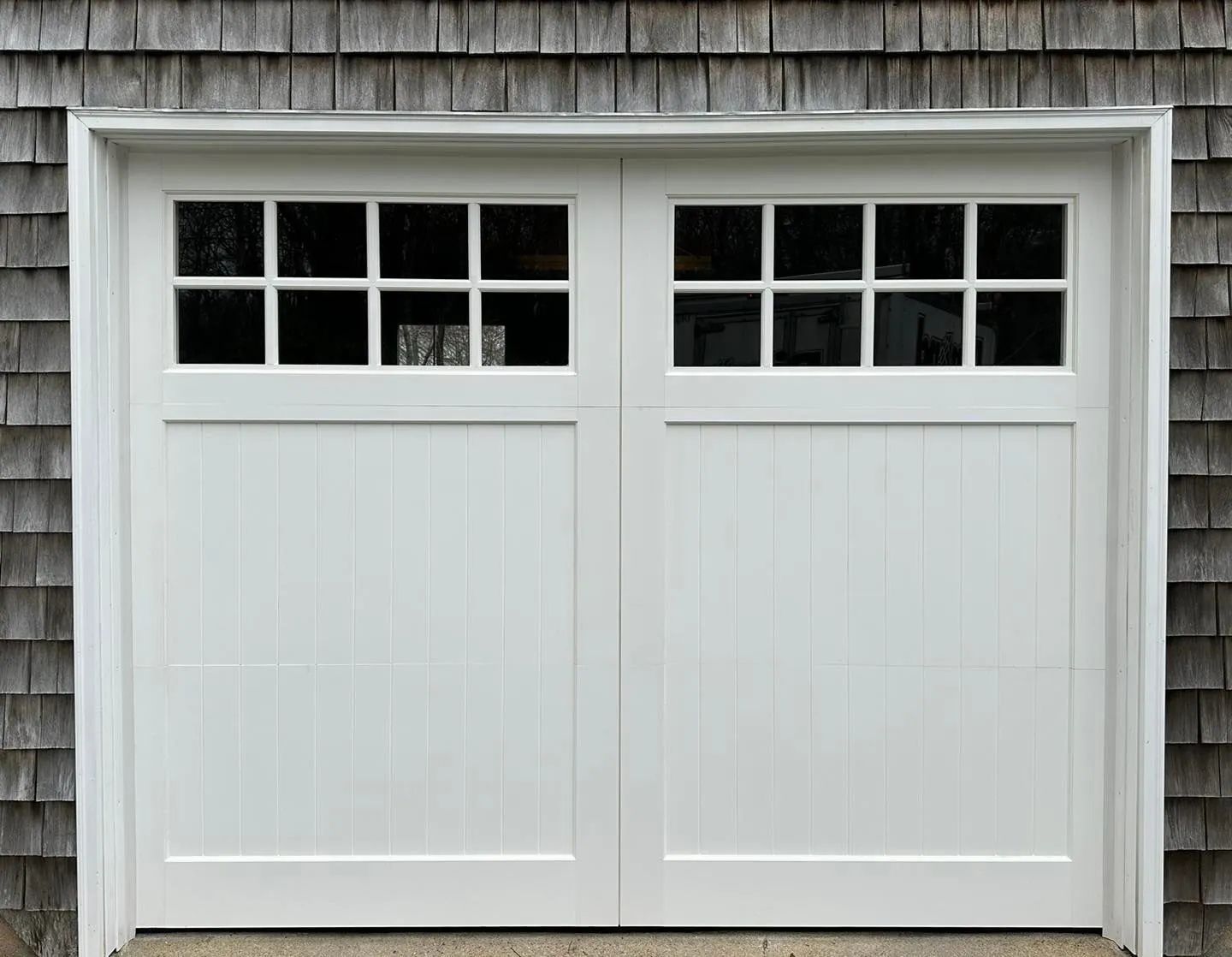 White double garage door with small window panes on top, set in a gray exterior wall.