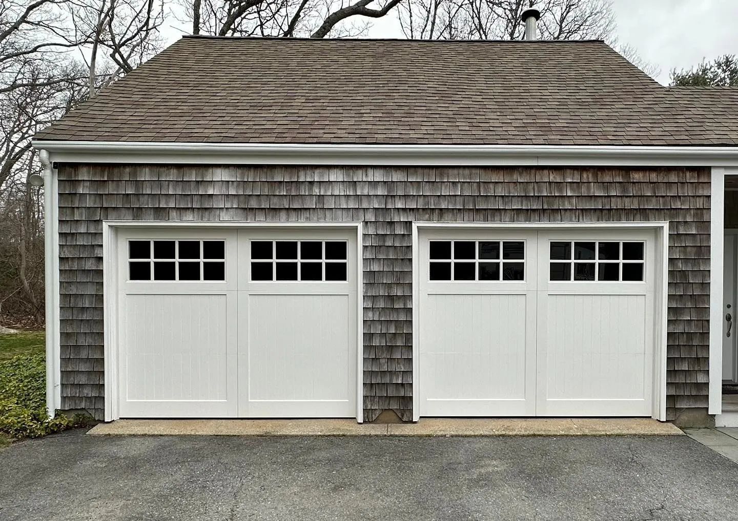 Two white garage doors on a gray shingled detached garage with a dark roof and driveway.