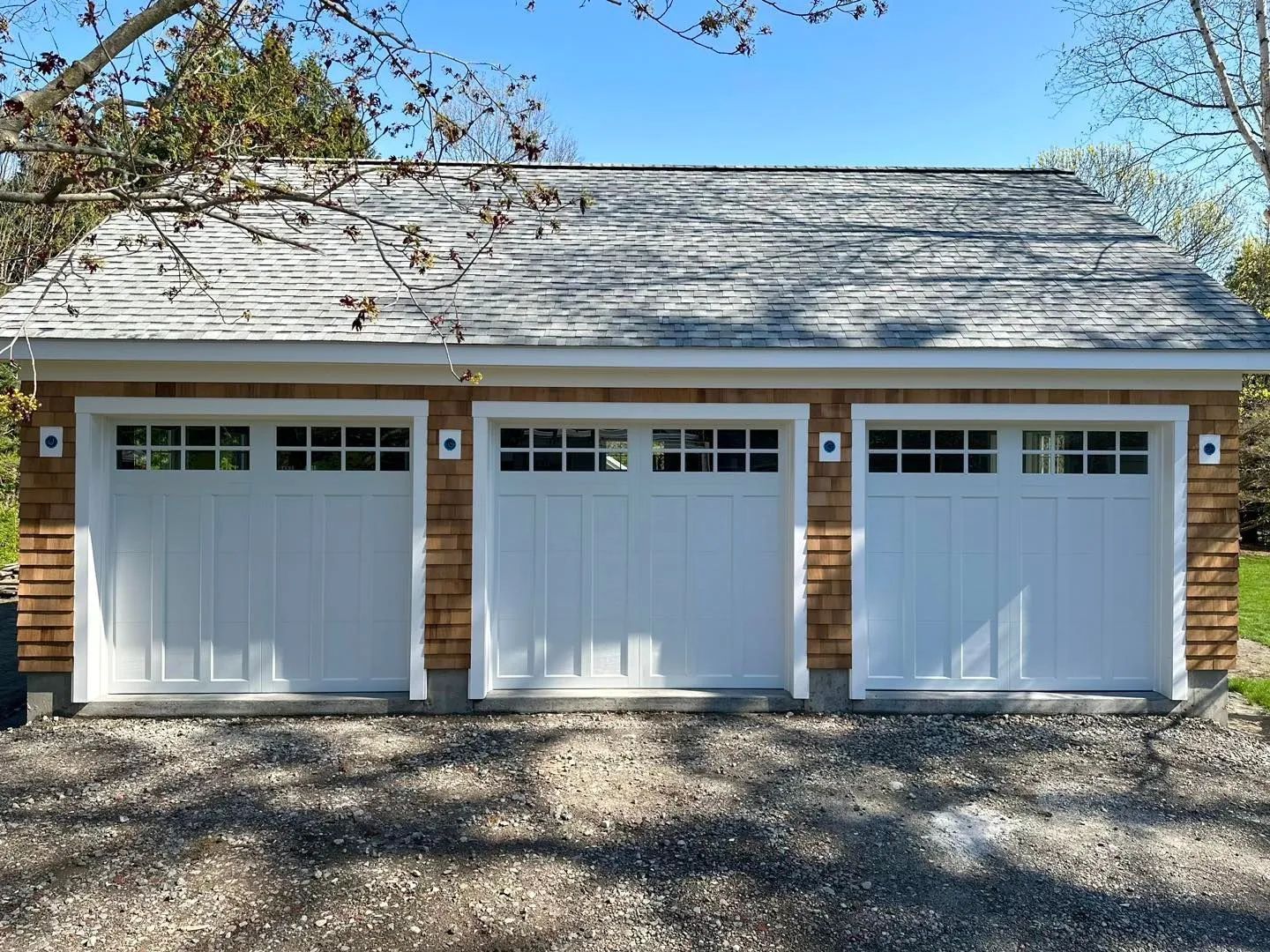 Three white garage doors on a brick house with a gray shingled roof and gravel driveway.