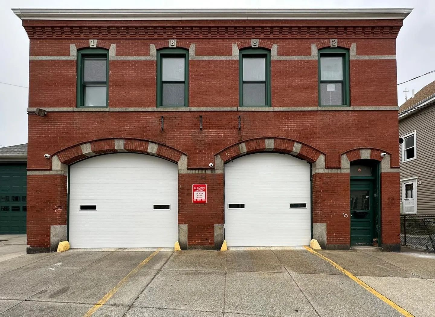 Brick firehouse with two white garage doors and arched entrances on a city street