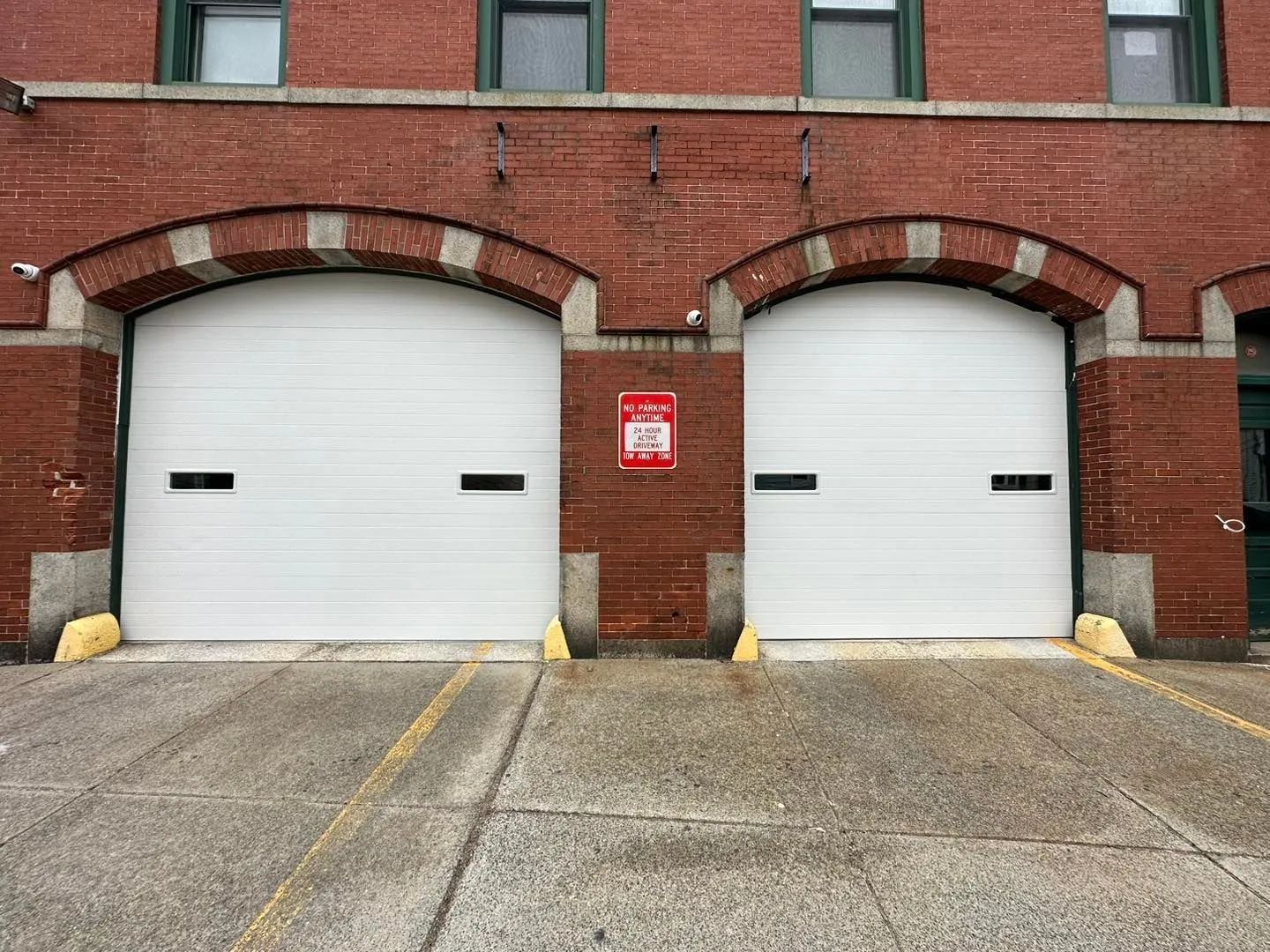 Two white garage doors in a red brick building with a red sign between them