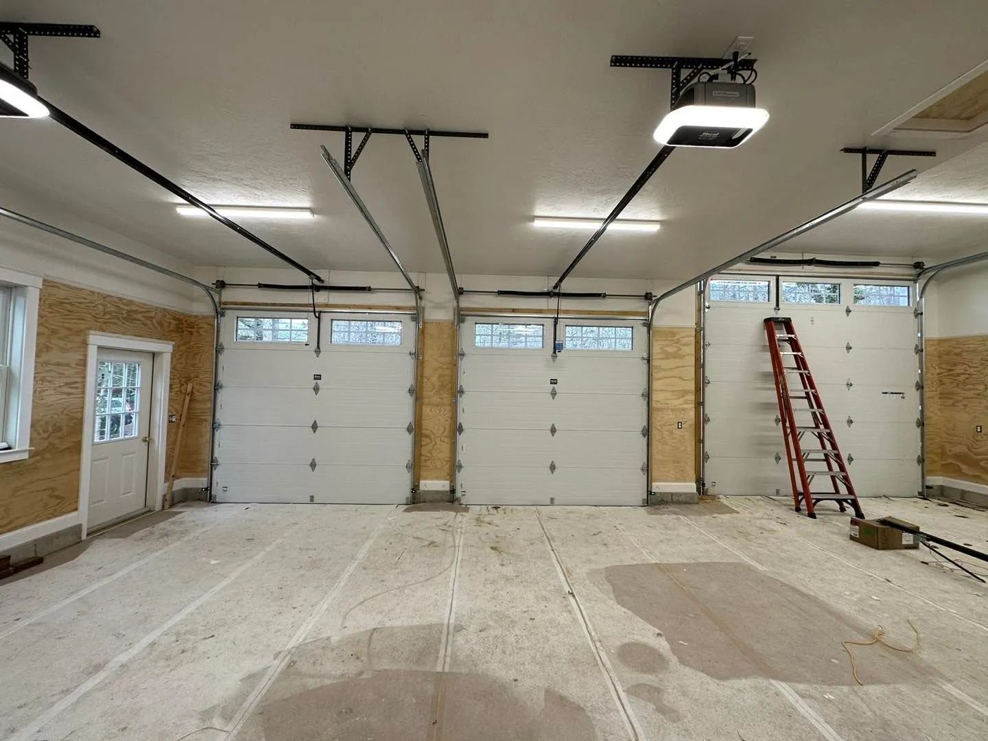 Partially finished garage with three white overhead doors and a red ladder on the right