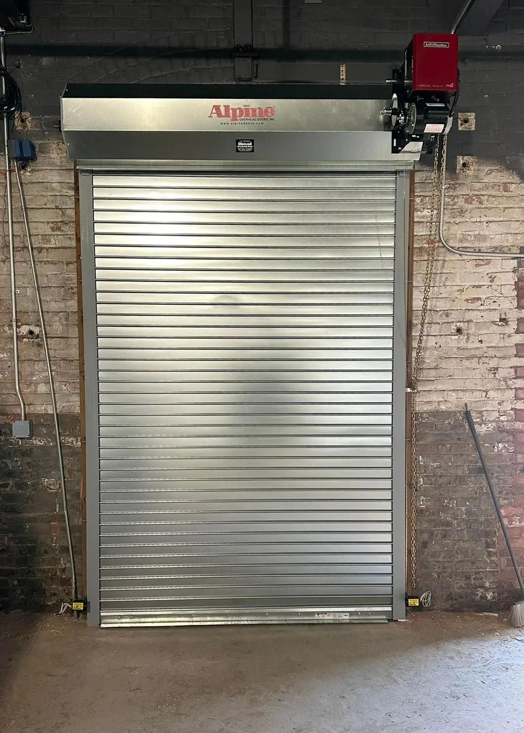 Closed silver roll-up warehouse door beneath an automated opener on a brick wall