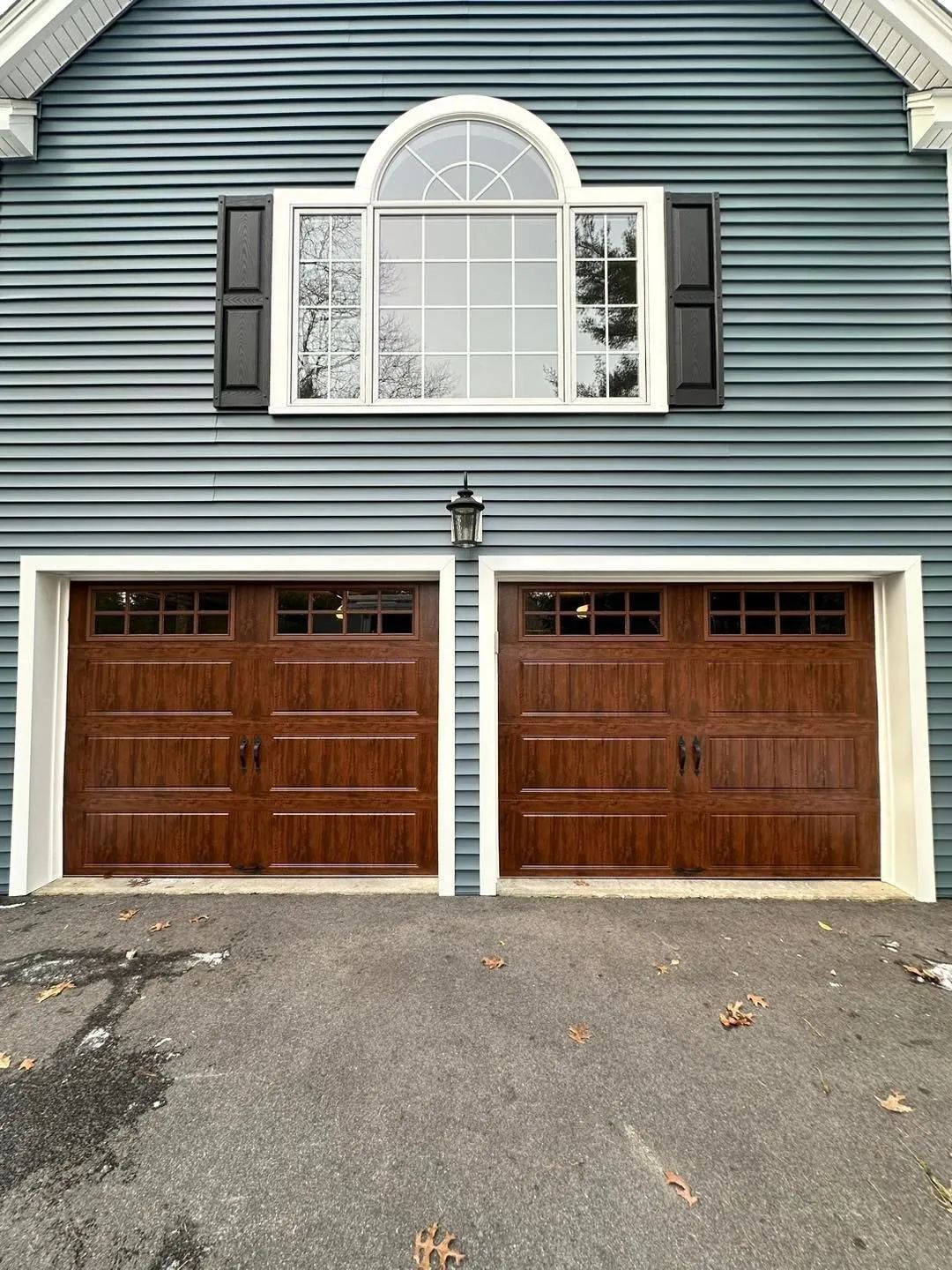 Two-car garage with brown doors beneath a blue house facade and arched window above