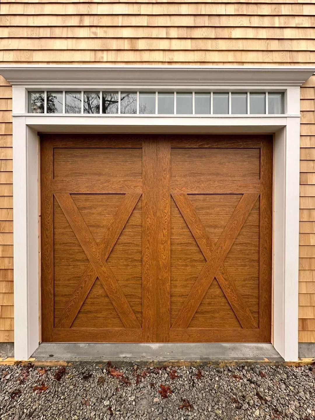 Wooden double garage doors with triangular panels in a beige shingled exterior wall