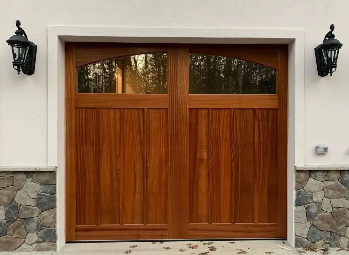 Wooden double garage door with narrow windows, set in a stone-and-stucco exterior wall with black lanterns