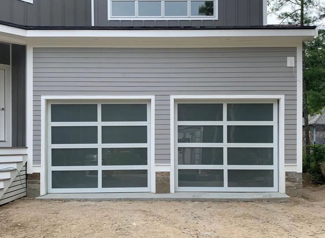 Two white garage doors with windows on a gray house exterior