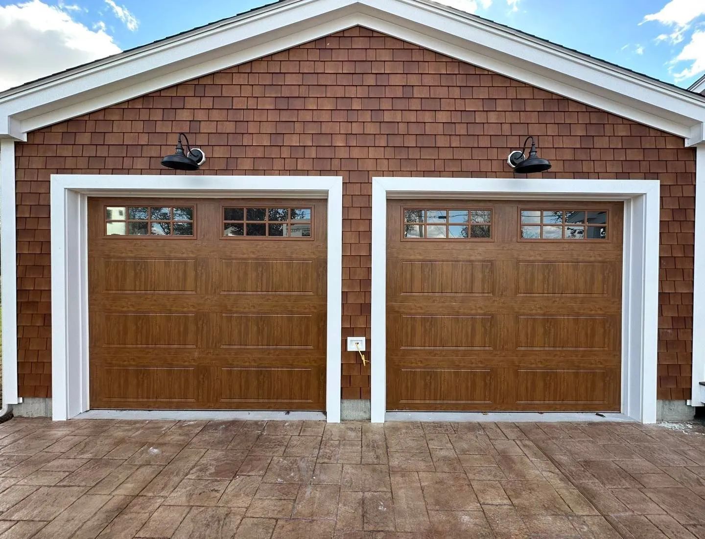 Two brown wooden garage doors on a brick house with white trim and a paved driveway