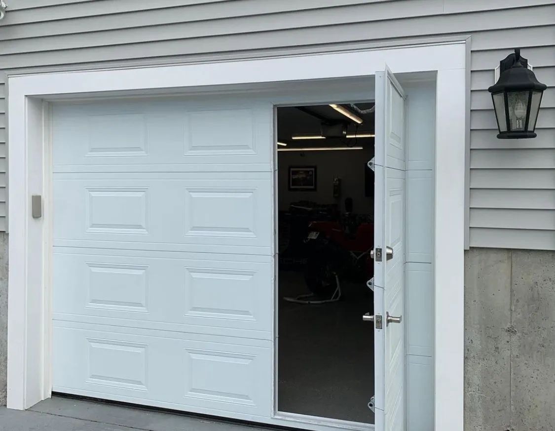 Open garage with a white overhead door and a side door ajar on a house exterior.