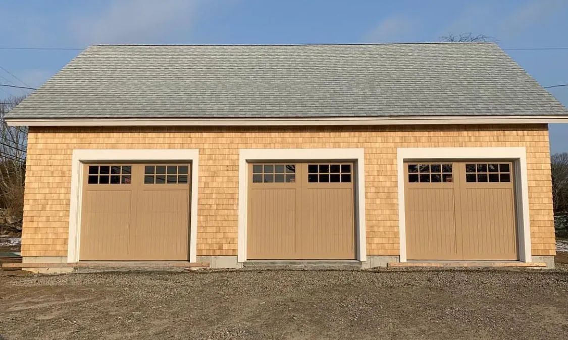 Three beige garage doors on a tan detached building with a gray shingled roof.