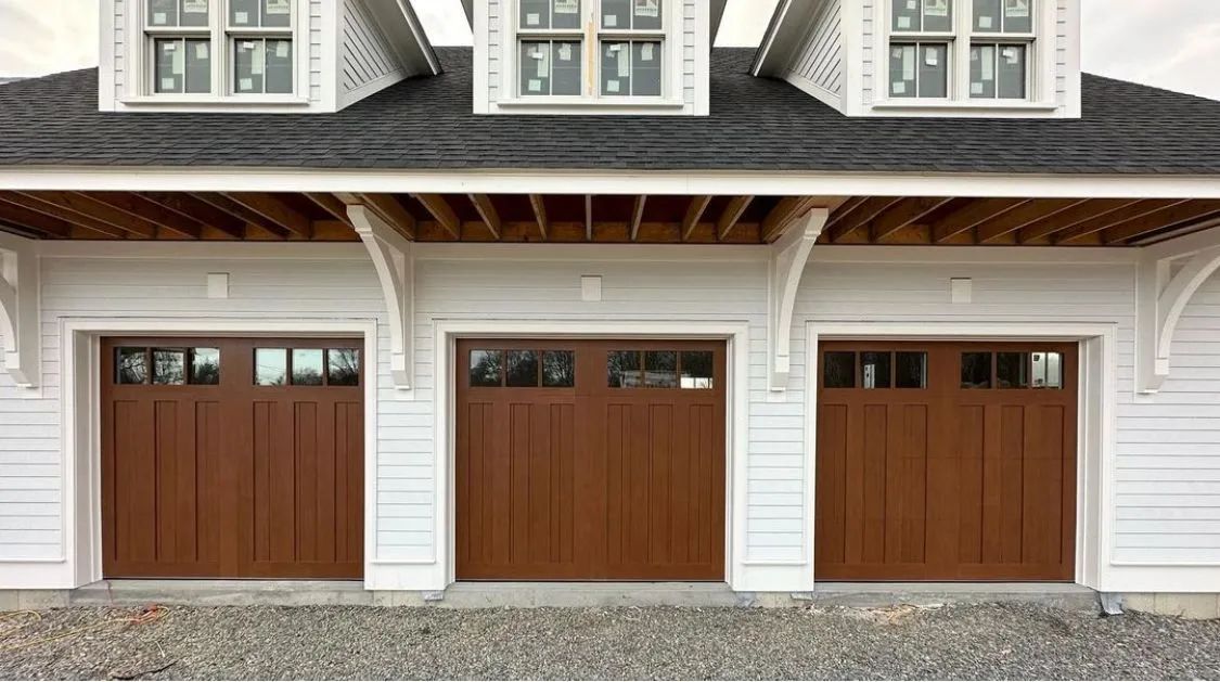 Three brown garage doors on a white house exterior under a porch roof