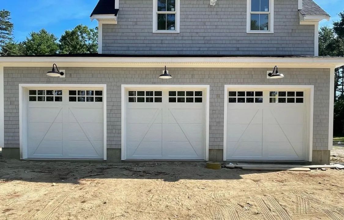 Three white garage doors on a house exterior with gray siding and gravel driveway