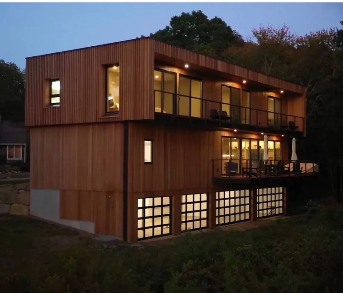 Modern two-story wooden house with large windows glowing at dusk