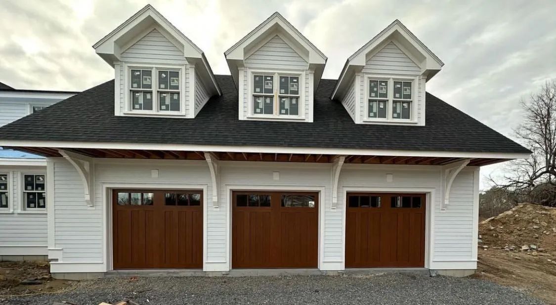 White three-car garage with brown wooden doors and three dormer windows on the roof