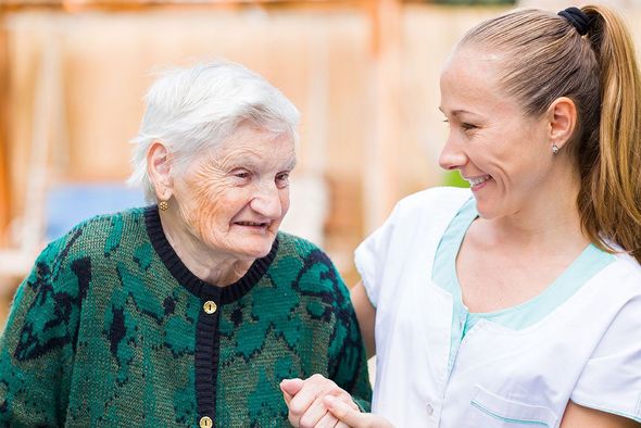 A nurse is holding the hand of an elderly woman.