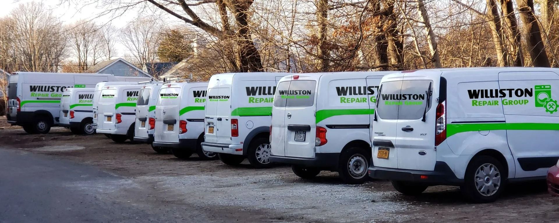 Row of white Williston service vans parked along a wooded road in autumn.