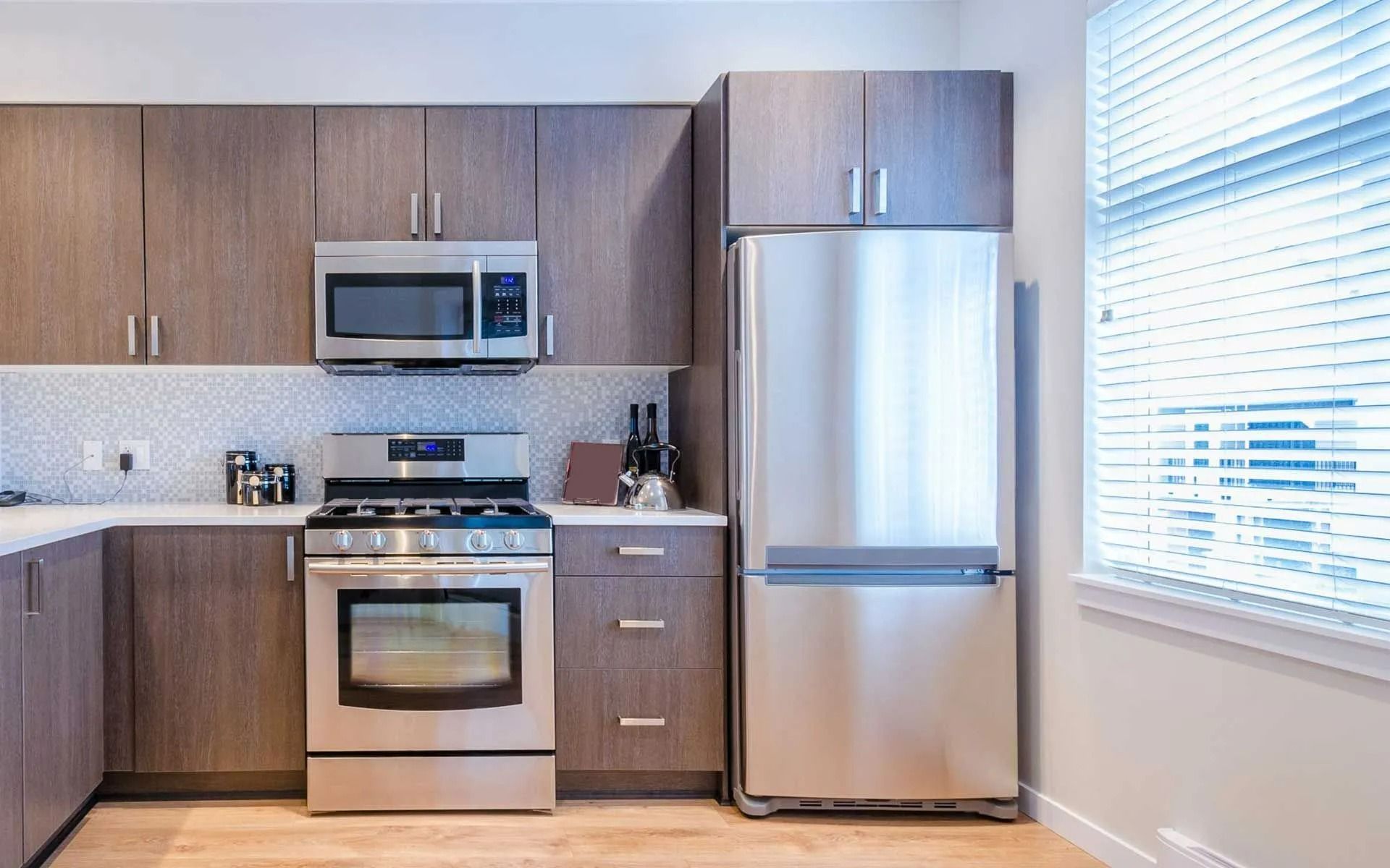 Modern kitchen with stainless steel appliances, wood cabinets, and a bright window.