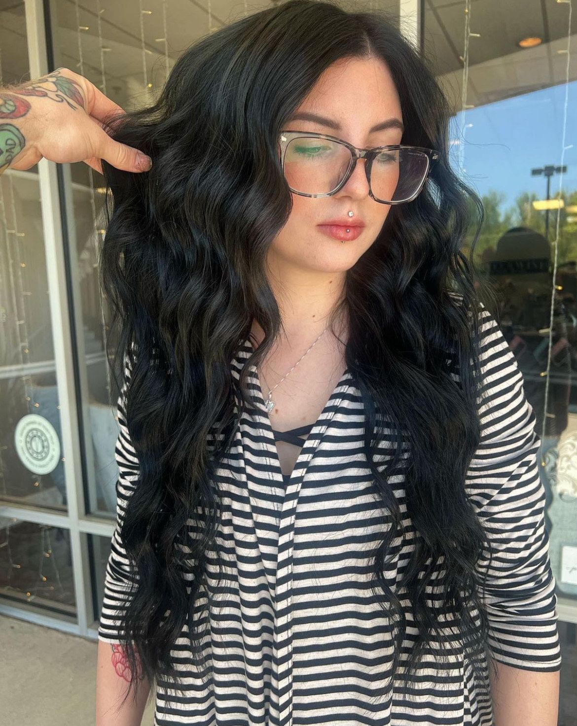 A woman with long black hair is wearing glasses and a striped shirt.