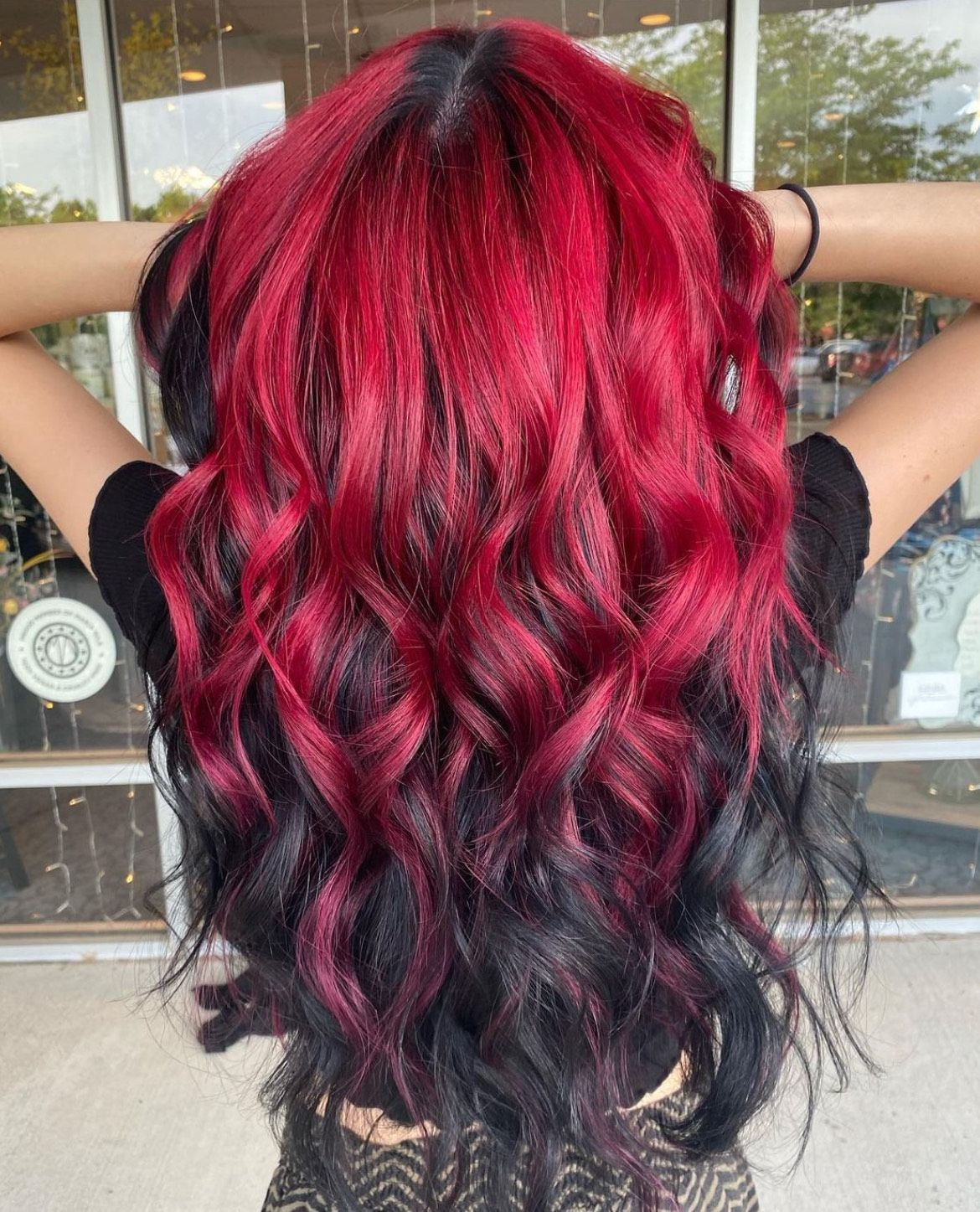 A woman with red and black hair is standing in front of a window.