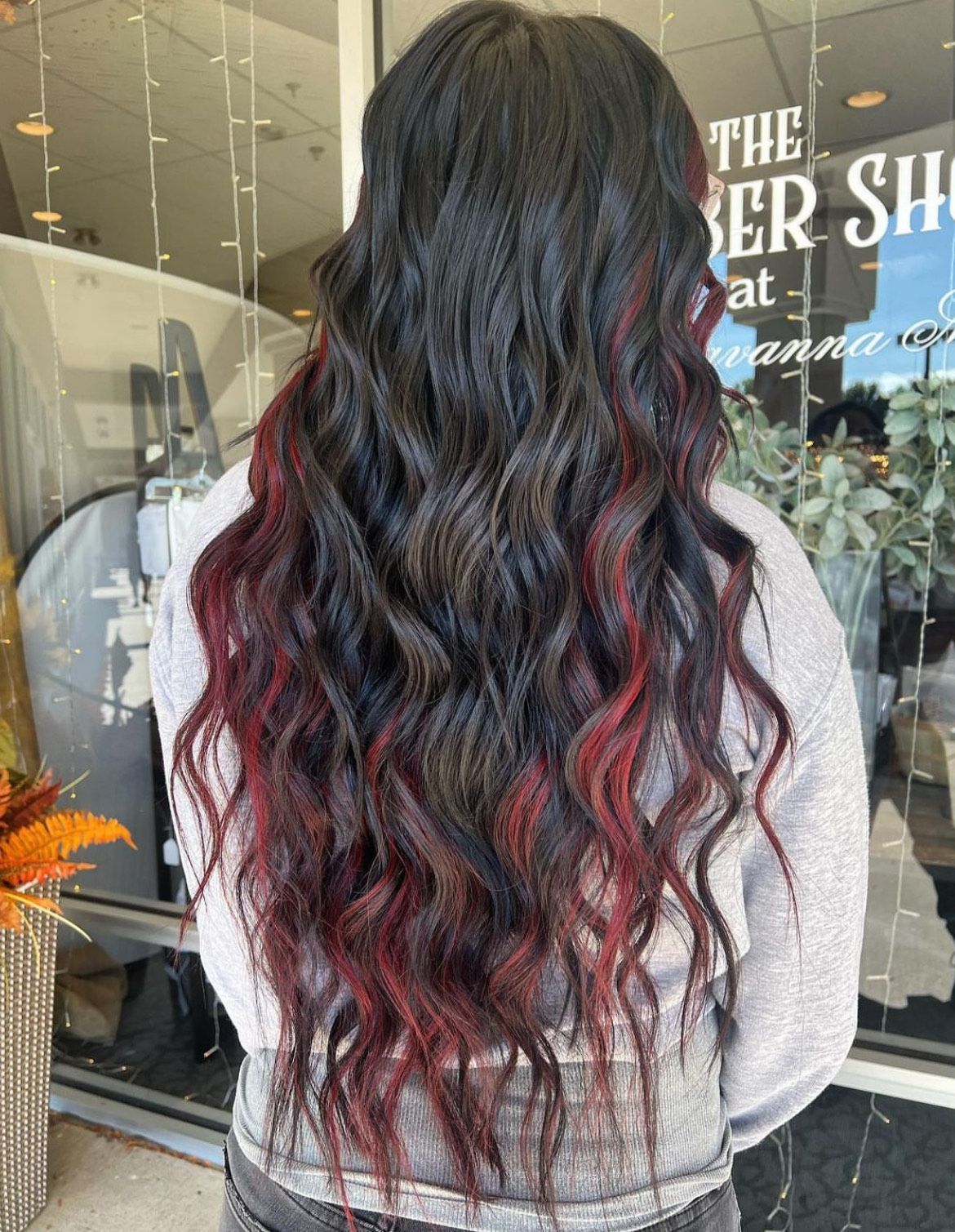 A woman with long black hair with red highlights is standing in front of a window.