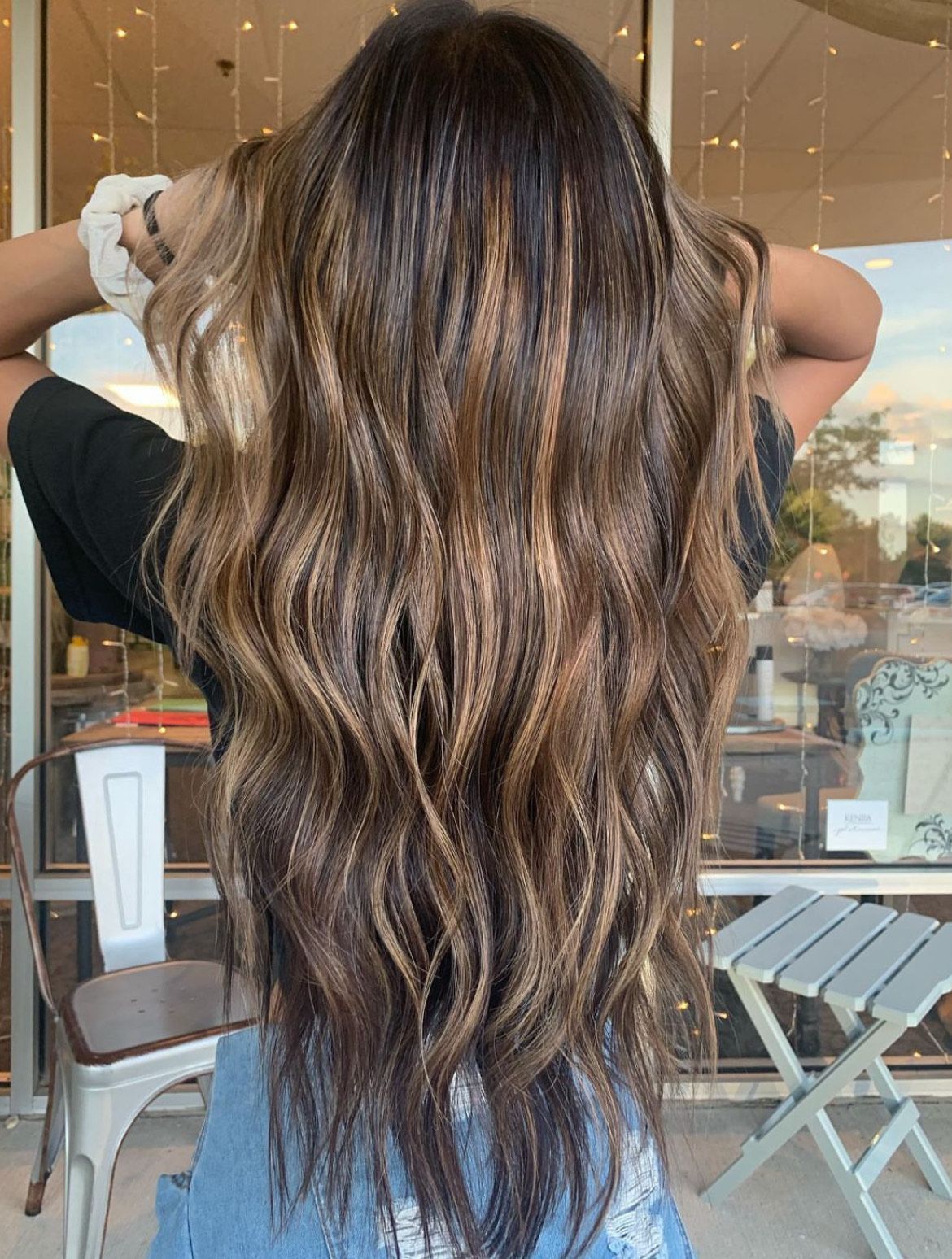 A woman with long hair is standing in front of a window with her hands in her hair.