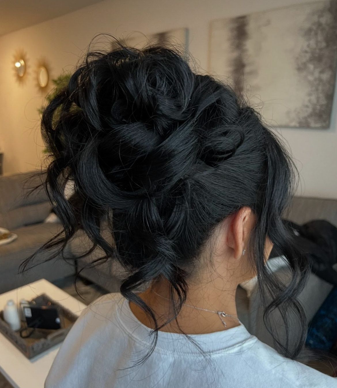 A woman with black hair in a messy bun is sitting in a living room.
