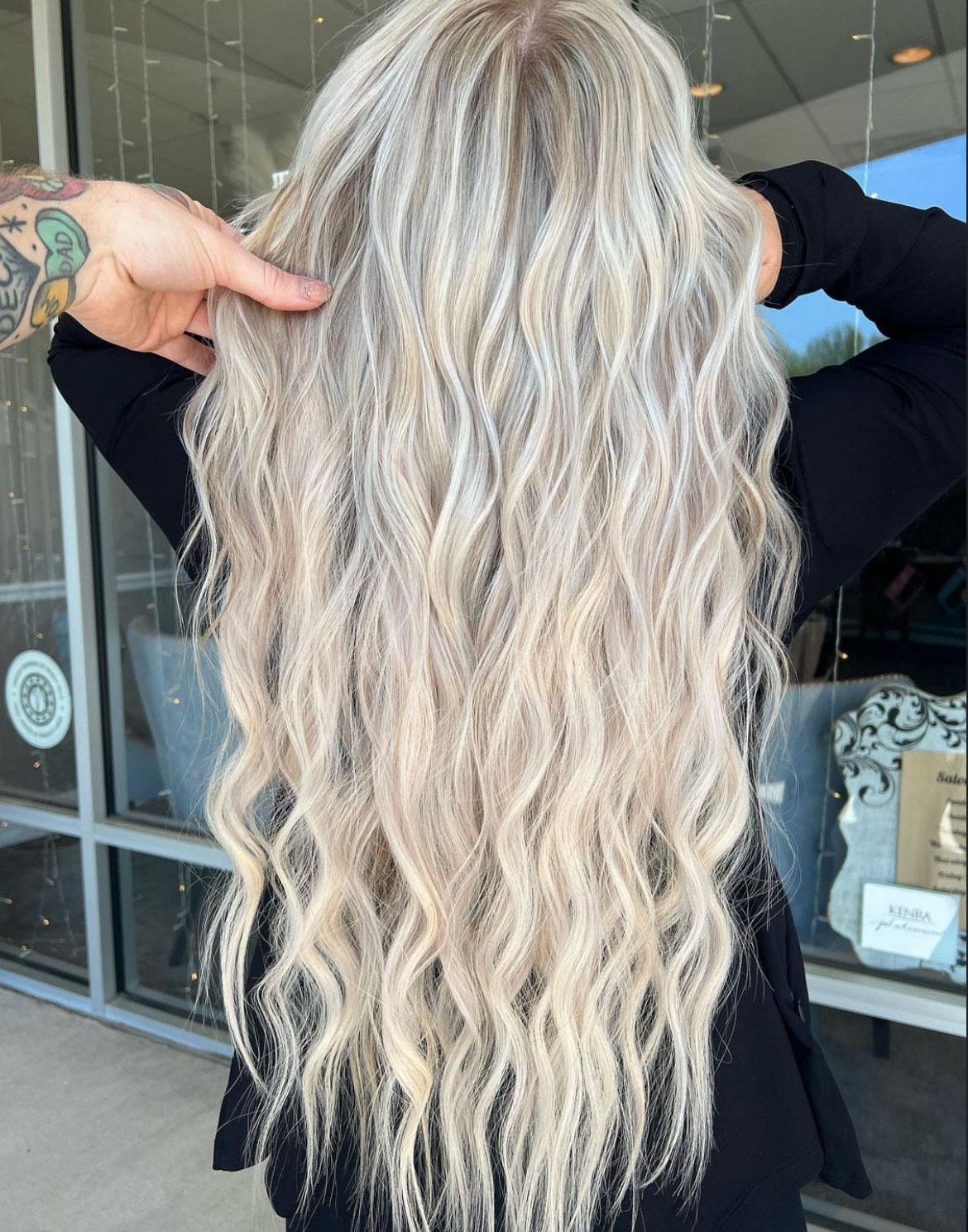 A woman with long blonde hair is standing in front of a window.