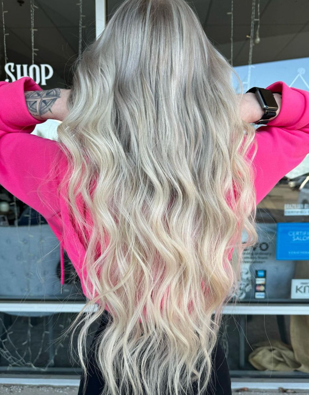 A woman with long blonde hair is standing in front of a window.